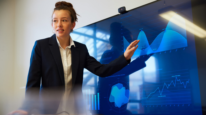 A person giving a presentation on a large TV screen displaying graphs.
