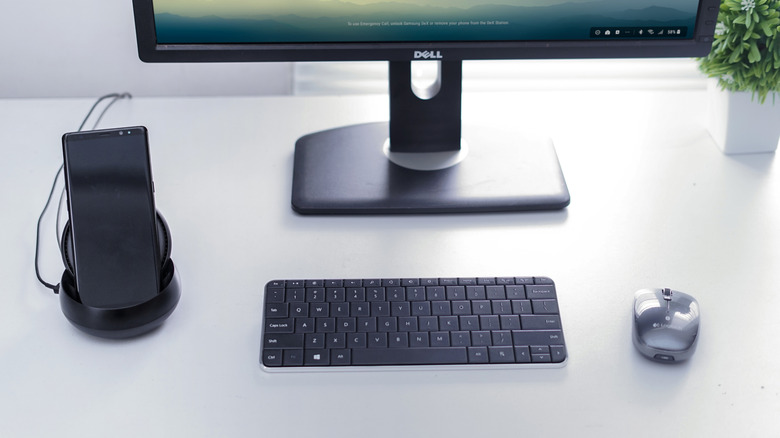 A Samsung phone in a DeX dock next to a connected monitor, keyboard, and mouse.