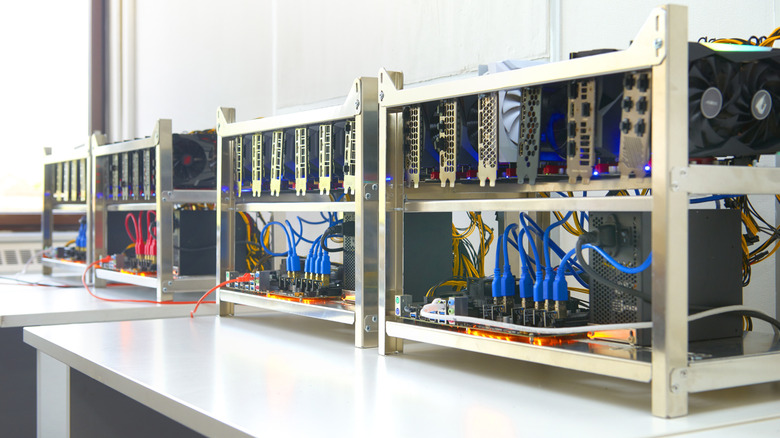 Rows of open-frame cryptocurrency mining rigs with multiple graphics cards and connected cables on a table.