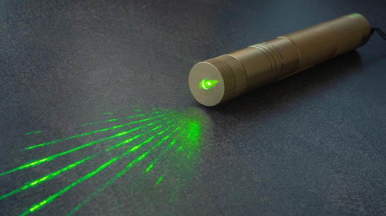 Close-up of a green laser pointer projecting bright laser lines onto a dark surface.