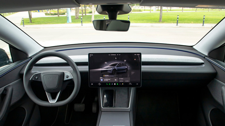 The interior of a Tesla Model Y, including the steering wheel, foot pedals, and infotainment screen