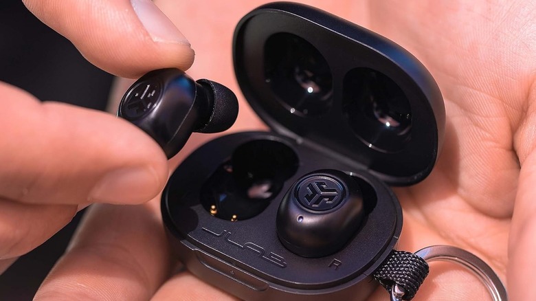 The JLab JBuds Mini wireless earbuds and their charging case on a person's palm.