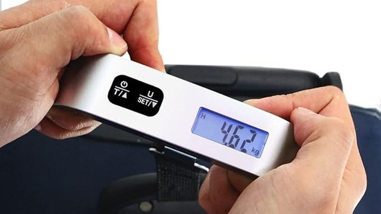 A person using the Travel Inspira luggage scale on a suitcase.