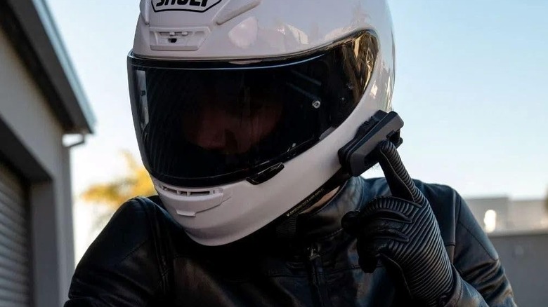 A motorcyclist presses a button on the side of their helmet.