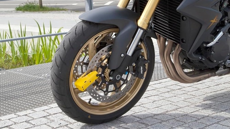 A bright yellow disc lock on a parked motorcycle.