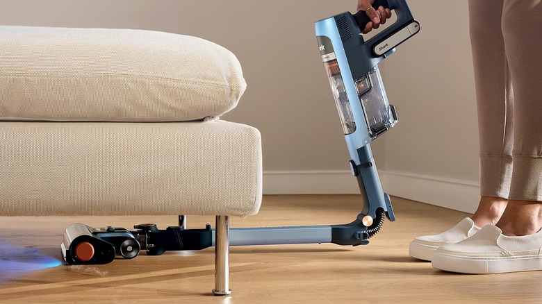 A person using the Shark PowerDetect Speed Clean and Empty cordless vacuum, flexing to clean underneath a couch.