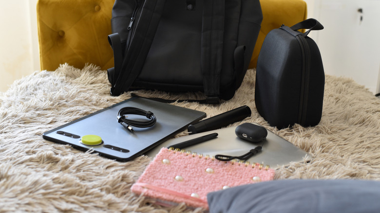 A graphics tablet, AirPods, USB-C cable, and other tech accessories placed on top of a flulffy rug with two bags in the background.