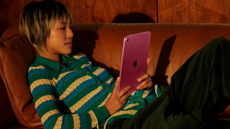 A person using the Apple iPad (A16, 256GB) tablet while on a couch.