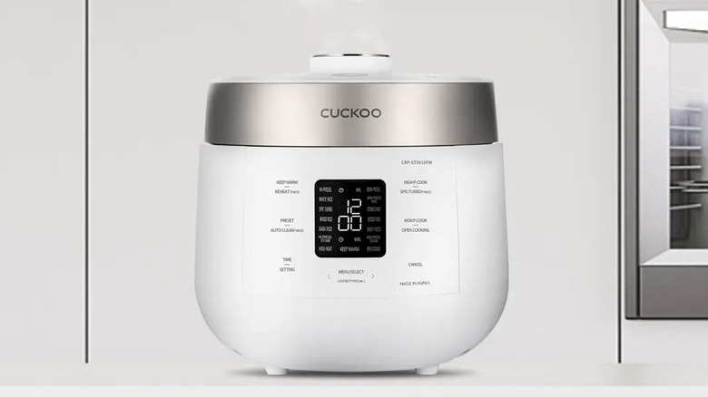 Cuckcoo 6-cup Twin Pressure Rice Cooker steaming on a modern kitchen countertop next to a wall oven.
