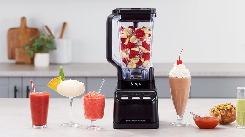Ninja Professional Blender with Auto-IQ filled with fruit on a kitchen counter surrounded by smooties.