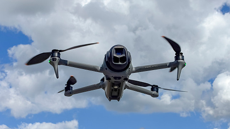 A drone in flight seen from below against a cloudy blue sky.