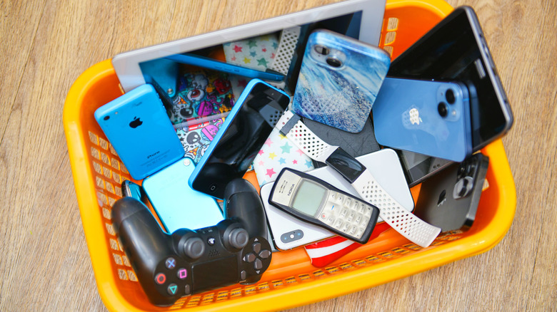 A plastic basket filled with used items including a smartphone and game controller.