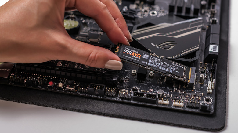 A hand installs an M.2 SSD into a slot on a computer motherboard.