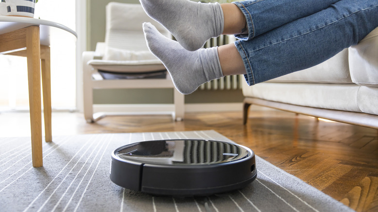 A person lifts their feet to let a robot vacuum pass.