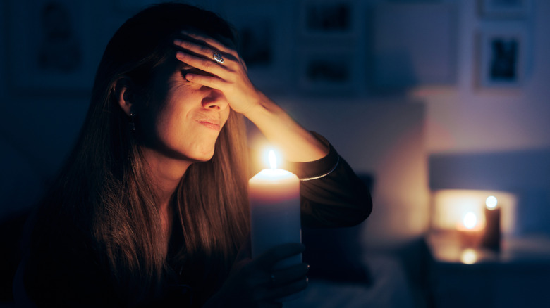 A frustrated woman sitting in a dark room that is illuminated only by candlelight.