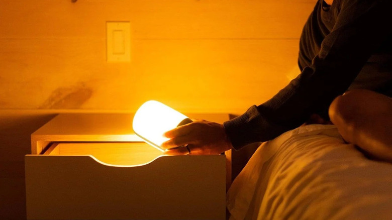 A person reaches in to a bedside drawer and pulls out the AlpenGlow 500 lantern, as it illuminates the room in warm whit elight