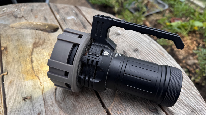 AceBeam X75 placed on a wooden cable drum inside a greenhouse with plants in the background; light is on and visible clearly in the daytime.