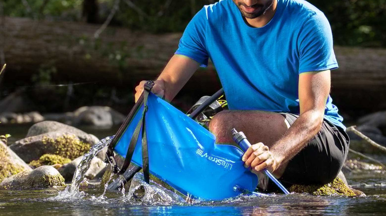 A man is refilling the LifeStraw gravity water filter from a stream
