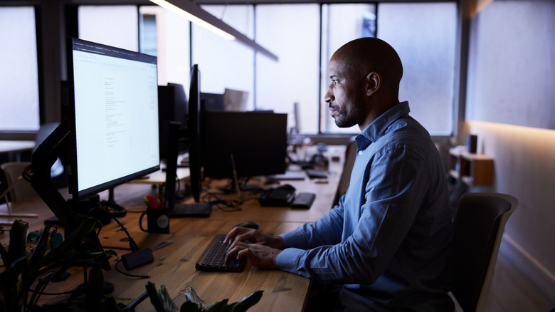 A man working on a computer in a dimly-lit office environment