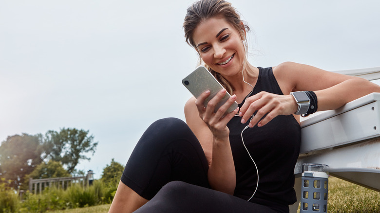 A woman using her phone while sitting on the grass after an outdoor run.