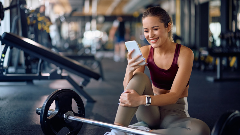 A woman looking at her phone while taking a break from weight training.