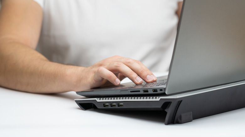 A man working on a laptop with a cooling pad placed underneath it.