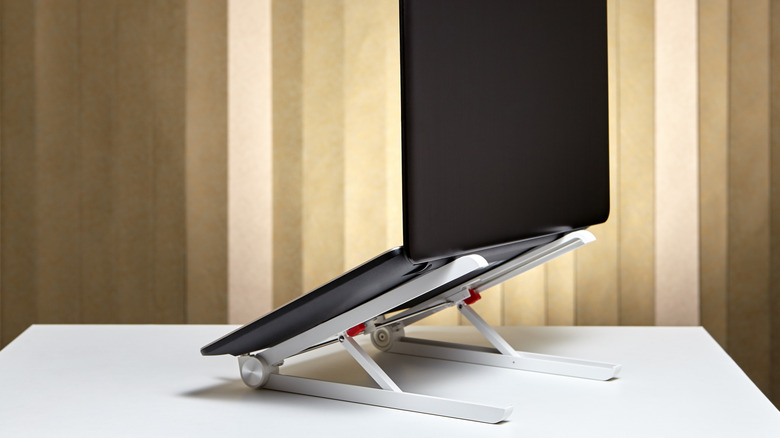A laptop holder suspending a laptop at an angle atop a white surface.