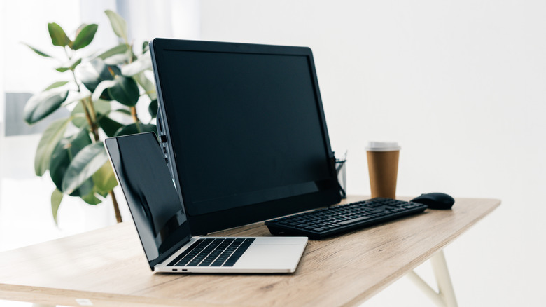 A laptop, a large portable monitor, and an external mouse and keyboard placed on a wooden desk.