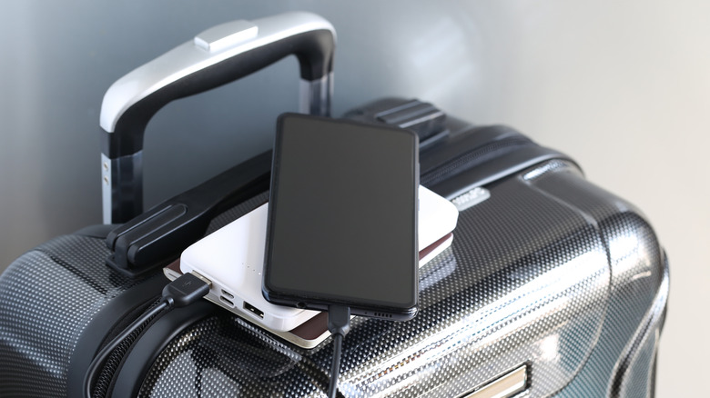 A power bank, phone, and charger on top of a silver piece of luggage.
