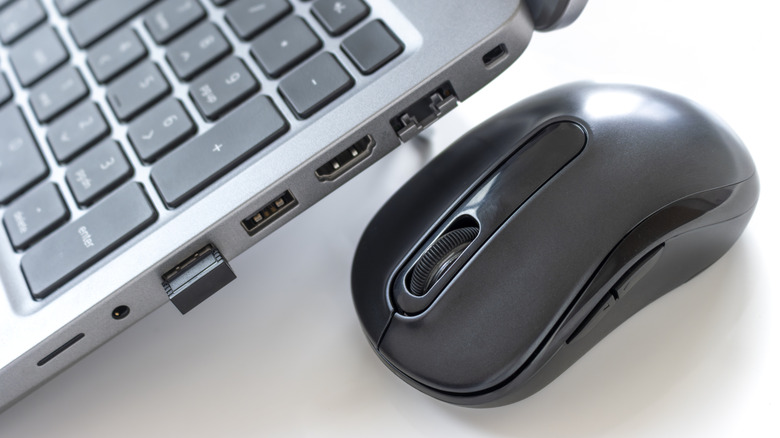 A black wireless mouse next to a silver laptop with a dongle plugged into its USB-A port.