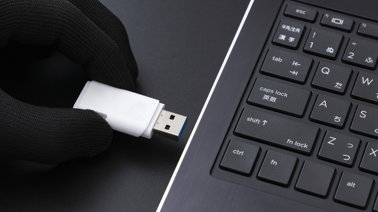 A gloved hand inserting a USB flash drive into a laptop.
