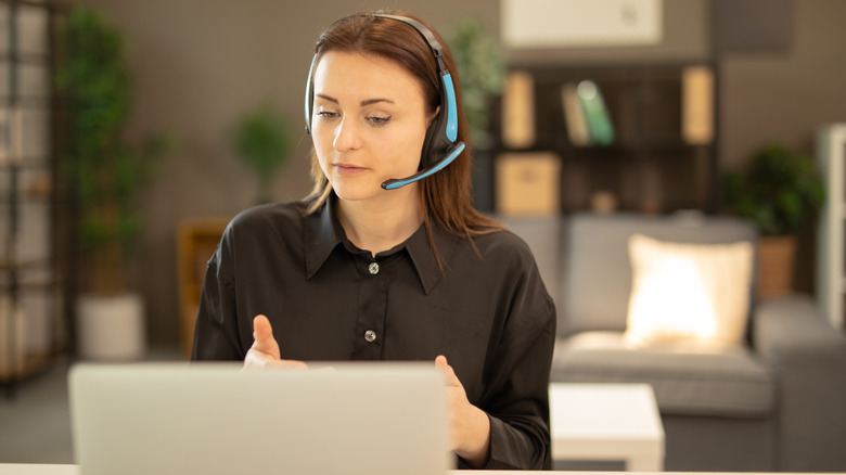 A woman wearing a headset while looking at her laptop in a living room.
