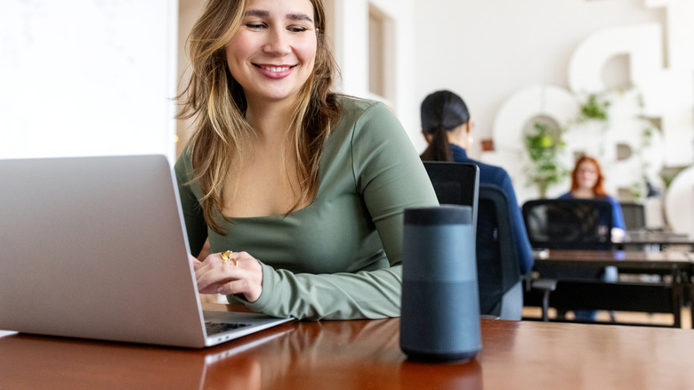 A woman smiling at a Bluetooth speaker placed next to her laptop.