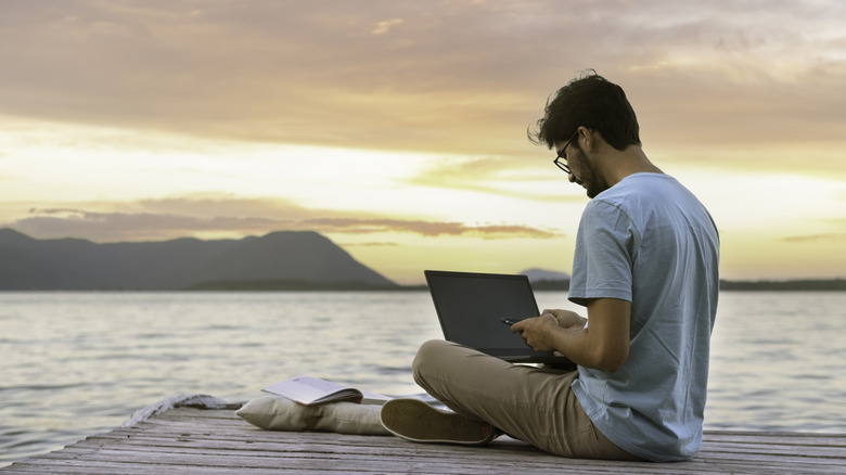 A person working on his laptop and phone while on a dock.