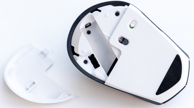 An upside down computer mouse with its battery compartment open and visible empty.