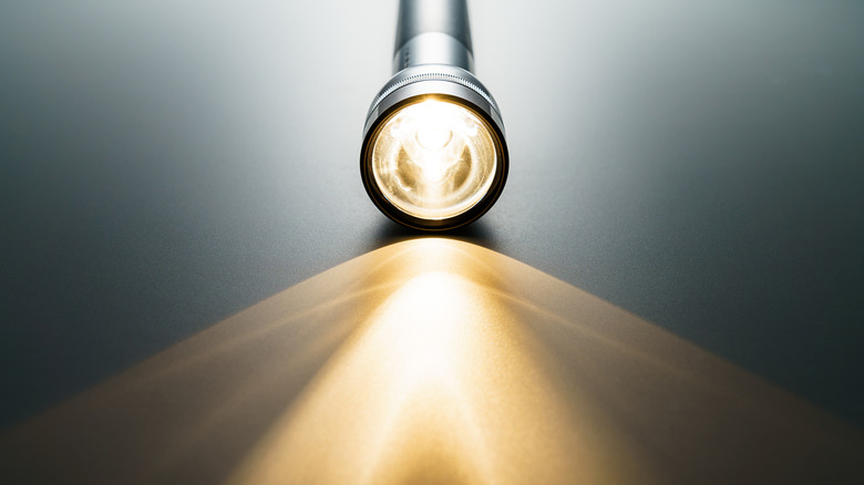 A flashlight shines its light on the table it's laying upon.