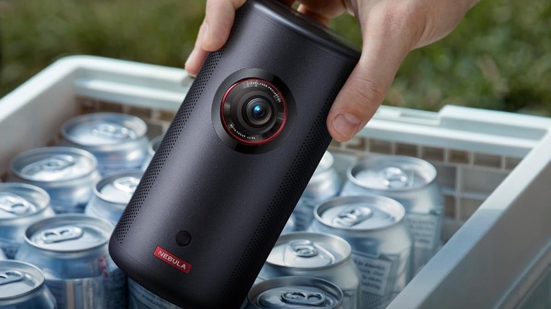 A person holding the Anker Nebula Capsule 3 portable projector next to cans of drink