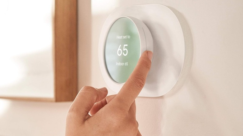 A hand adjusting the thermostat temperature on a white wall