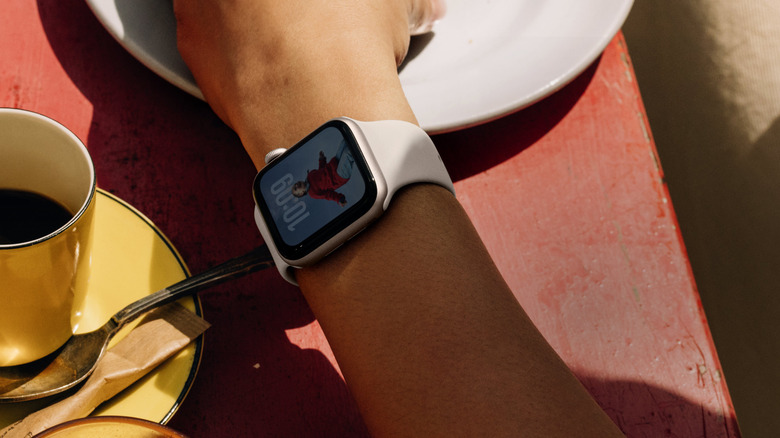 A hand with a smartwatch strapped on resting on a table
