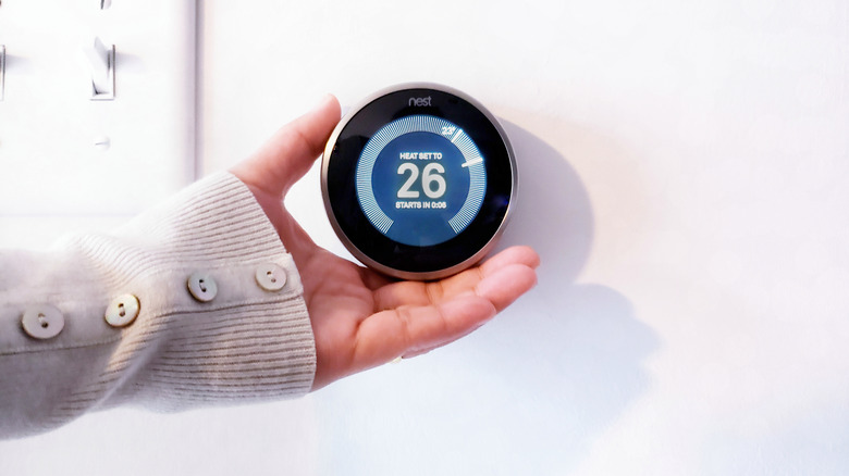 A hand holding the nest thermostat on a white wall