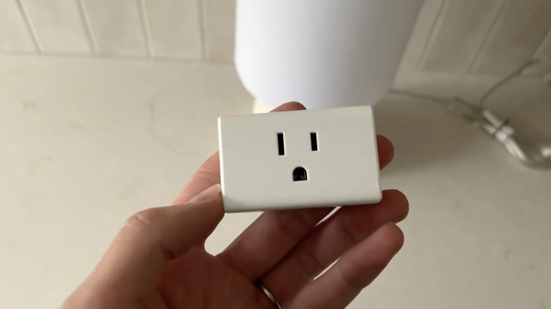 A hand holding a smart plug in a white background