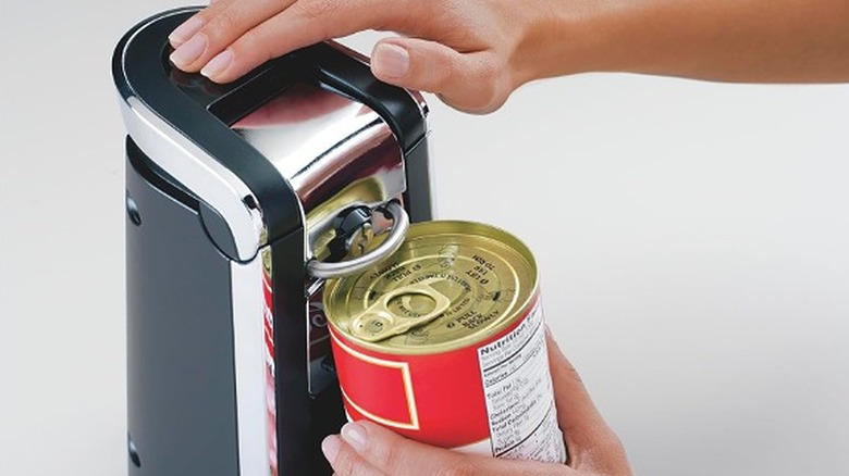 A set of hands operating the Hamilton Beach Smooth Touch Electric Can Opener to open a can.