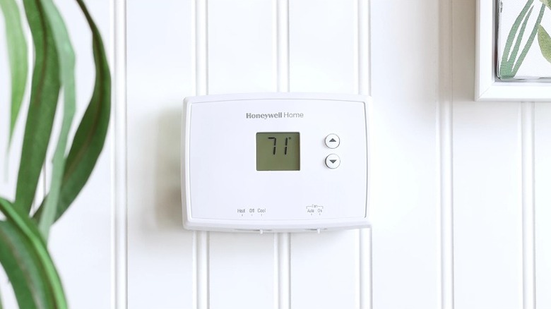 A white Honeywell Home Horizontal Non-Programmable Thermostat placed on a white wall.
