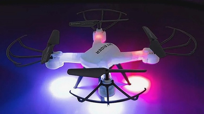 A white Sky Rider Pro Quadcopter Drone with its lights turned on against a dark purple-pink background.