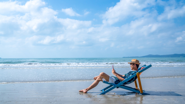 A person looking at his phone while sitting on a chair on a beach.