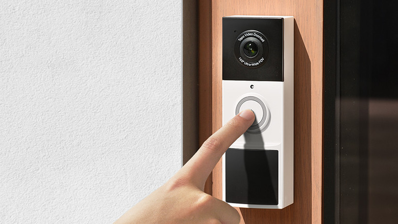 A finger pressing the button of the Tapo D210 video doorbell.