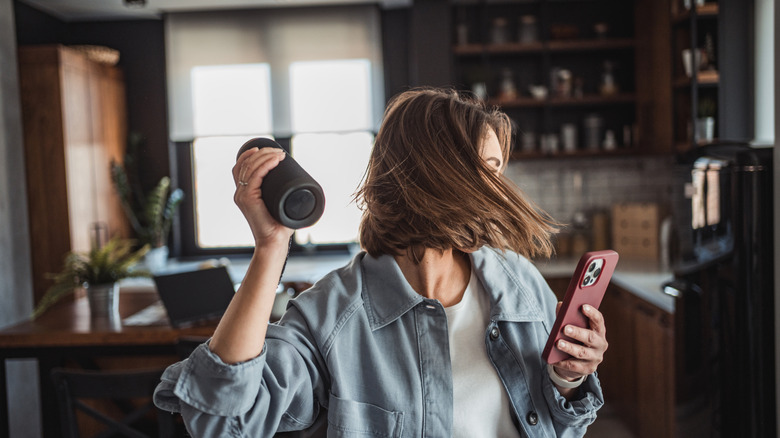 A woman dancing with a phone and Bluetooth speaker in her hands