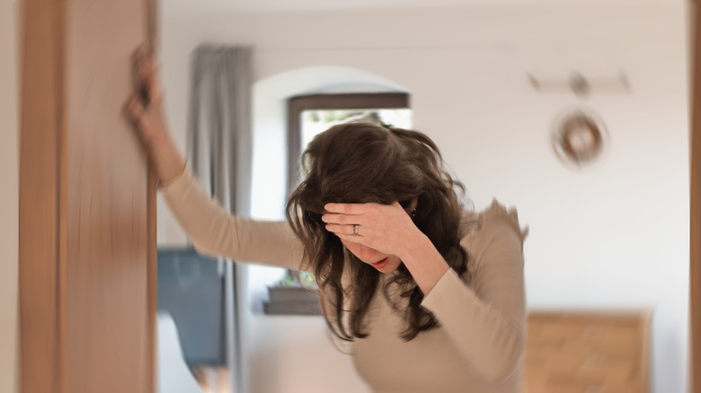 A woman grabbing onto wall an holding her head while room spins