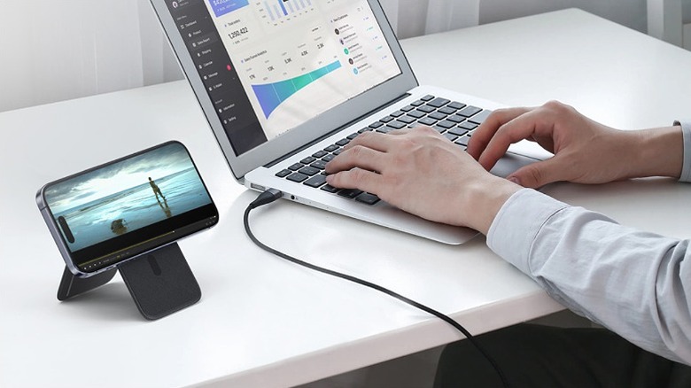 Man working on a laptop with a video playing on an iPhone on the side,