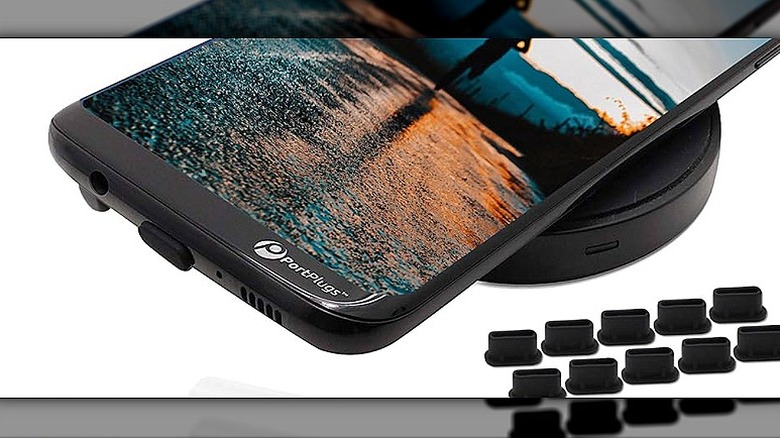 Several USB-C dust plugs placed beside a phone mounted on a wireless charger.